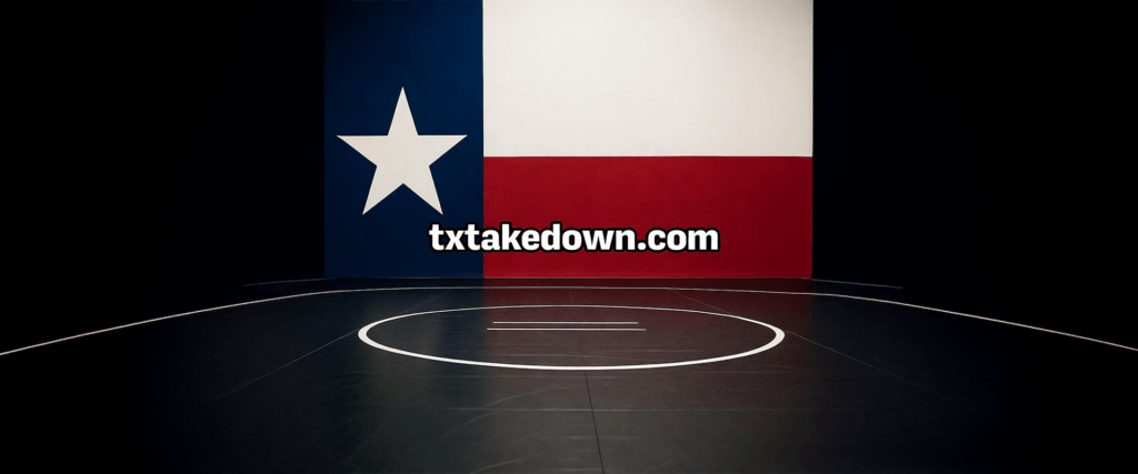 A wrestling mat in a gym is centered against a wall featuring the Texas flag. The website "txtakedown.com" is displayed on the flag.